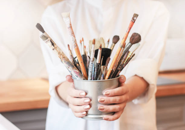 istock Different brushes in metal bucket with artist hands, selective focus 1028104366