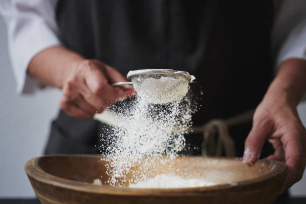 Female hands sifting flour to bowl. Slow motion shot of aged female hands sifting flour by sieve in wooden bowl. confectioner photos stock pictures, royalty-free photos & images