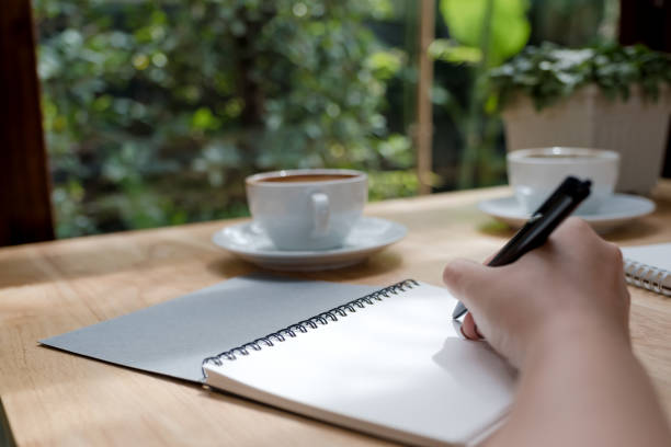 istock Closeup image of a hand writing down on a white blank notebook with coffee cup on wooden table 1028142850