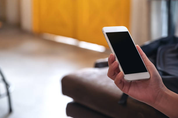 istock Mockup image of hands holding white mobile phone with blank black screen in cafe 1028143044