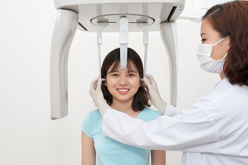 Professional doctor taking care of young girl in office making panoramic dental x-ray with special facility
