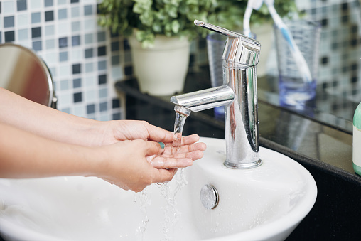 Crop shot of woman in bathroom washing hands in sink with clear stream of water