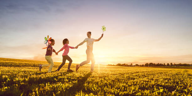 mother and two daughters are playing on meadow Happy loving family is having fun on nature in the summer. Young mother and two daughters are laughing and playing on meadow at sunset background. happy sibling day stock pictures, royalty-free photos & images