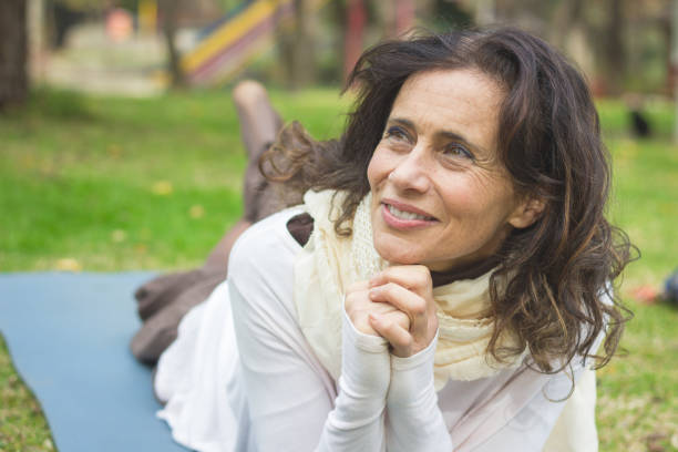 beautiful mature lady smiles lying down on mat in the park with optimistic look in her eyes - idealist imagens e fotografias de stock