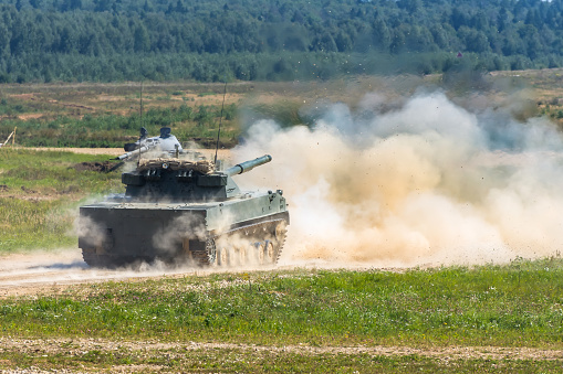 The military tank makes a shot at the enemy targets in the field