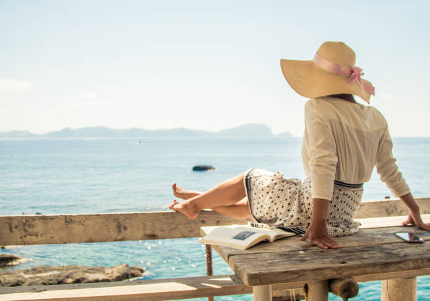 mujer joven sentada en el balcón de madera en la isla de palmarola frente al mar en un día soleado. elegante vestido blanco con falda y sombrero - one person beautiful barefoot beach fotografías e imágenes de stock