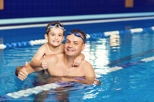 Young father and his little son having fun in an indoor swimming pool.