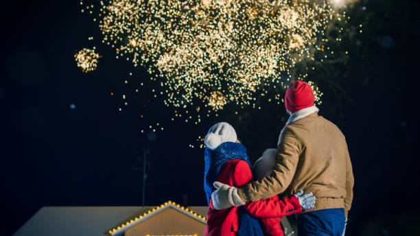 happy new year celebration, young family of three standing in the front yard watching beautiful fireworks. in the evening while snow is falling father, mother and cute little daughter look up in wonder. house decorated with garlands for christmas eve. - happy kid flash imagens e fotografias de stock