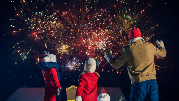 happy new year celebration, young family of three standing in the front yard watching beautiful fireworks. in the evening while snow is falling father, mother and cute little daughter look up in wonder. house decorated with garlands for christmas eve. - happy kid flash imagens e fotografias de stock