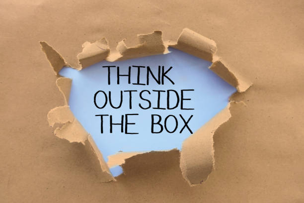 istock Think outside the box saying or advice  handwritten on white page,  behind torn brown paper or cardboard 1028224562