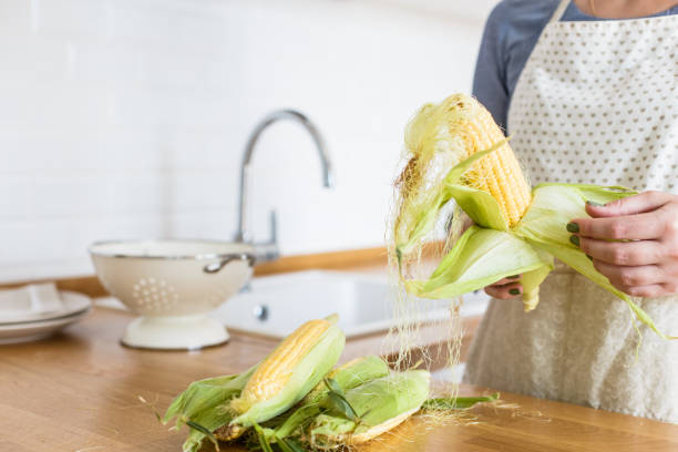 istock Woman holding colander with yellow corn cobs. View on white modern scandinavian style kitchen 1028237640
