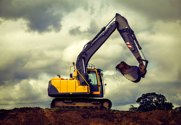 Yellow digger on hill lifting dirt against a dramatic cloudy sky stock photo