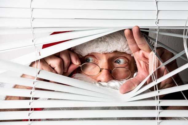 Santa Clause peeks through a window blind stock photo