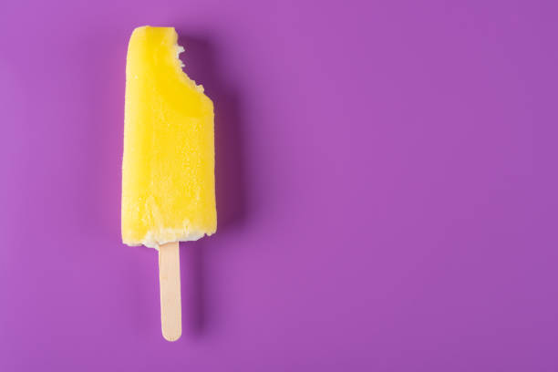 istock yellow popsicle with a bite on a purple background 1028278216