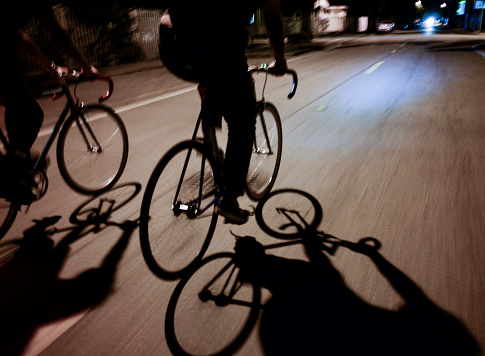 Shadows of 2 people riding bicycles in motion with contrasting light and dark shadows at night.
