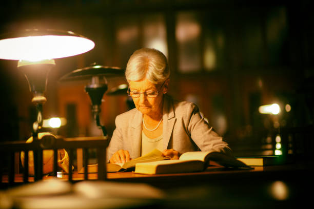 istock Senior woman reading in library at night 1028300954