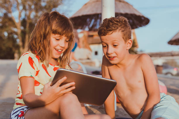 Kids playing with digital tablet on sandy beach Portrait of positive children playing with digital tablet together on sandy beach. kindle and ook stock pictures, royalty-free photos & images