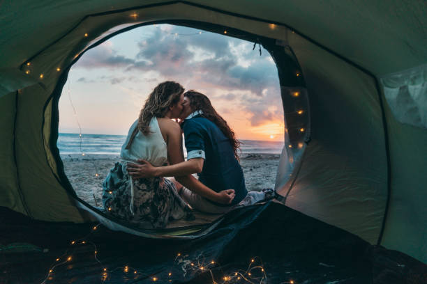 молодая взрослая пара любуясь закатом в палатке на пляже - lesbian homosexual kissing homosexual couple стоковые фото и изображения