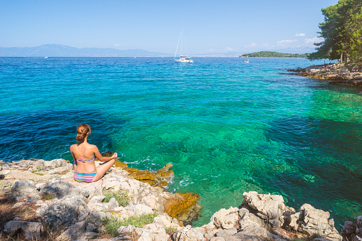 Young woman practicing morning meditation in nature at the beach. Caucasian woman practicing yoga at seashore near Malinska on island Krk, Croatia.