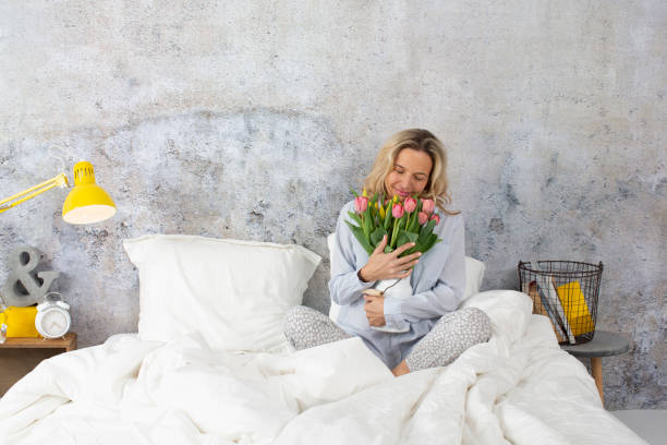 istock Smiling Woman Holding Bouquet While Sitting On Bed At Home 1028348038