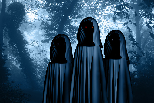 Three spooky monsters in hooded cloaks with glowing eyes in misty forest landscape. Photo toned in blue color