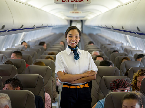 Portrait of a beautiful African American flight attendant in an airplane looking at the camera smiling - travel concepts