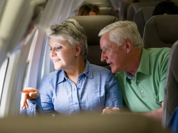 Portrait of a happy Latin American senior couple traveling by plane for their holidays and looking through the window