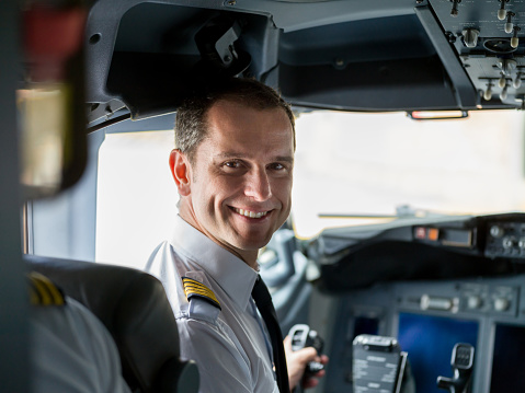 Portrait of a happy pilot in the airplane's cockpit looking at the camera smiling before take off - travel concepts