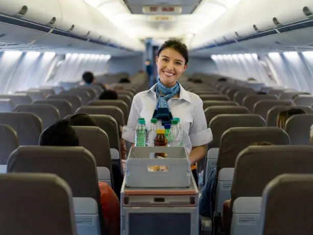 Portrait of a friendly flight attendant serving food and drinks in an airplane and looking at the camera smiling - travel concepts