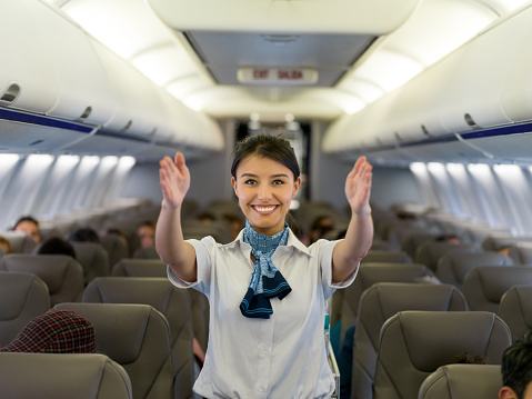 Portrait of a beautiful flight attendant showing the emergency exit in an airplane before takeoff - travel concepts