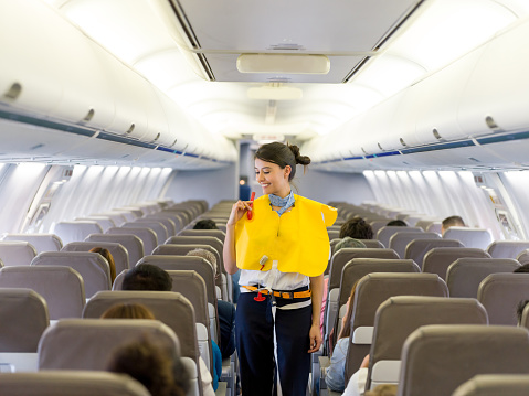 Portrait of a beautiful flight attendant making an in-flight safety demonstration and showing how to put the life vest