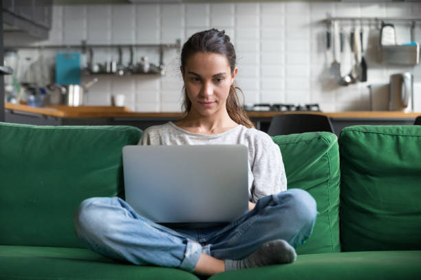 istock Serious woman using laptop checking news online sitting on sofa 1028379270