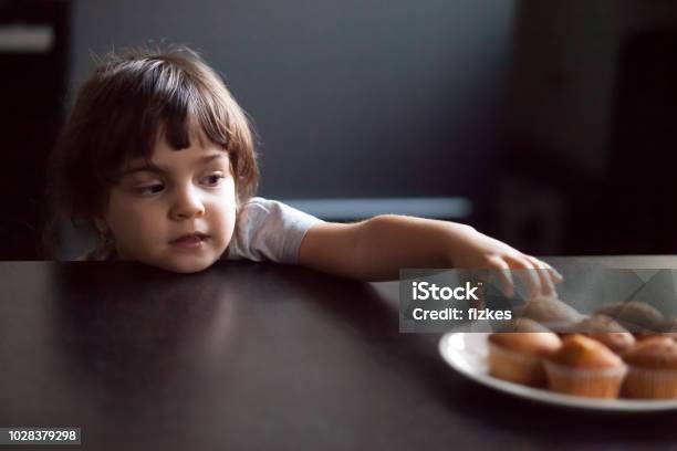 Cunning Cute Little Girl Stealing Delicious Muffin On Table Stock Photo - Download Image Now