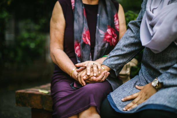Consolation from a friend Senior Chinese woman and adult Malaysian woman wearing hijab,having fun outdoors nervous holding hands stock pictures, royalty-free photos & images