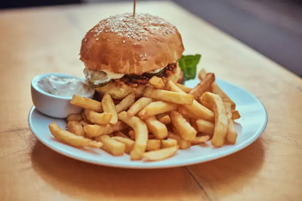 Photo of Close-up image of a hamburger with French fries and spicy sauce on a white plate. Unhealthy food concept