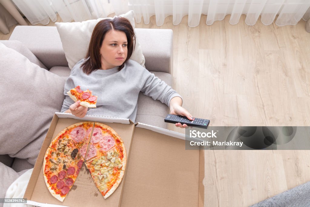woman eating pizza image taken from above Woman laying on couch with cell phone eating pizza Eating Stock Photo