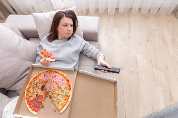 woman eating pizza image taken from above Woman laying on couch with cell phone eating pizza laziness stock pictures, royalty-free photos & images