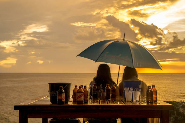 Two women at table with Red Stripe Beer Negril, Jamaica - May 30 2015: Two caucasian women sitting at table with Red Stripe Beer holding an umbrella looking at the sunset in Negril, Jamaica. 1974 stock pictures, royalty-free photos & images