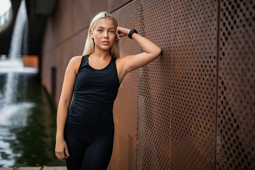 Portrait of fit young woman in sportswear leaning on metallic wall after workout