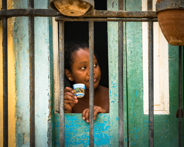 Woman in Havana watches the world go by from her colorful window as she sips from an equally colorful coffee cup.