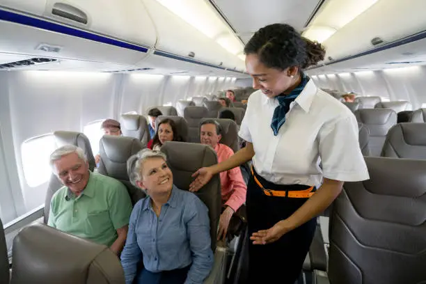 Friendly flight attendant checking on a senior couple in an airplane and looking happy - travel concepts