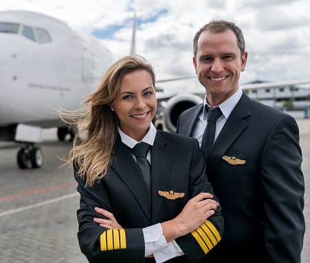 Portrait of a team of successful pilots next to an airplane and looking at the camera smiling - travel concepts