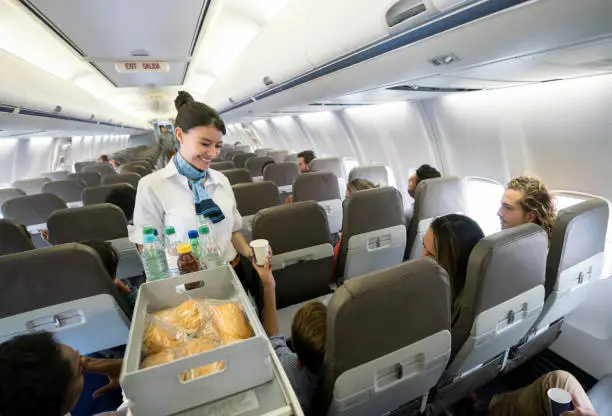 Portrait of a friendly air stewardess serving food and drinks onboard and smiling - travel concepts