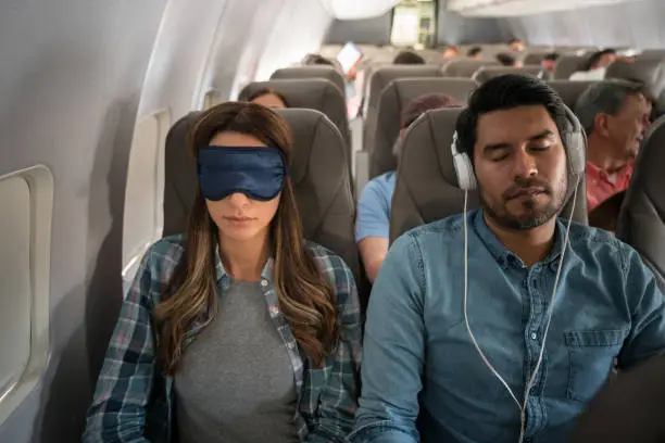 People traveling by air and sleeping on the plane wearing headphones and an eye mask - travel concepts