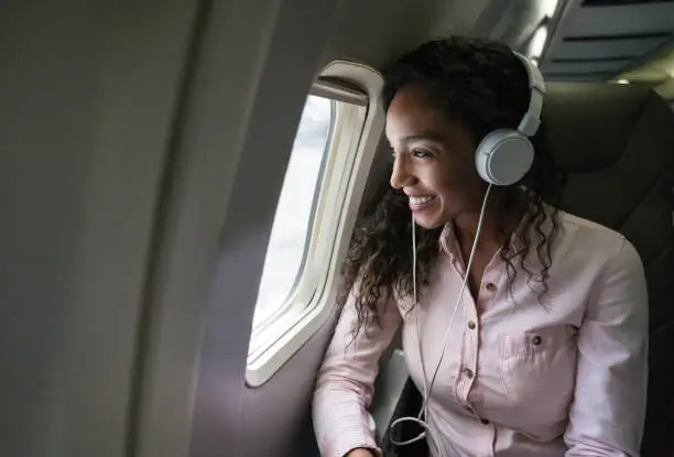 Portrait of a happy African American woman traveling by plane and listening to music on her cell phone using headphones - lifestyle concepts