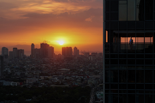 Young businessman with digital tablet in hand standing in office in Manila at sunset