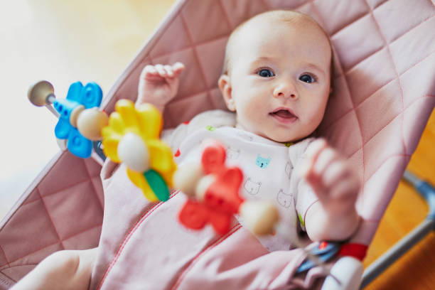 Baby girl sitting in bouncer and playing with colorful toys stock photo