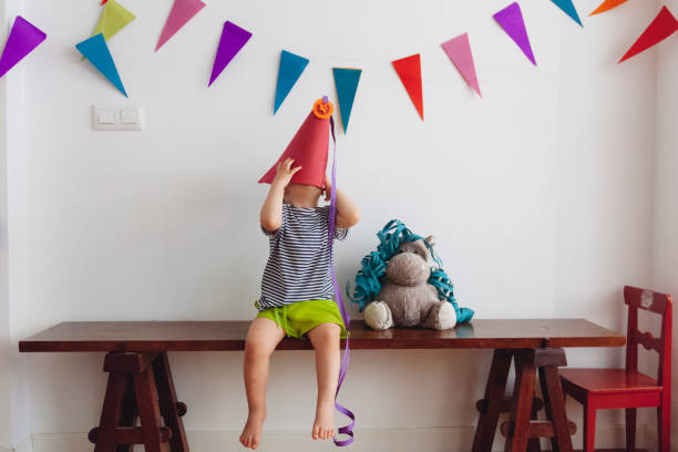 маленький ребенок играет с днем рождения дома сделал шляпу - kid made стоковые фото и изображения