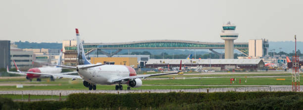 GATWICK AIRPORT, ENGLAND, UK – AUGUST 30 2018: Norwegian Airlines planes prepare to take off from Gatwick Airport GATWICK AIRPORT, ENGLAND, UK – AUGUST 30 2018: Norwegian Airlines planes prepare to take off from Gatwick Airport overlooked by the air traffic control tower and aeroplane bridge. gatwick airport photos stock pictures, royalty-free photos & images