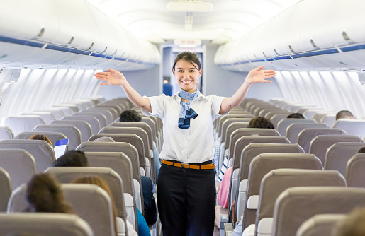 Portrait of a beautiful flight attendant showing the emergency exit in an airplane before takeoff - travel concepts